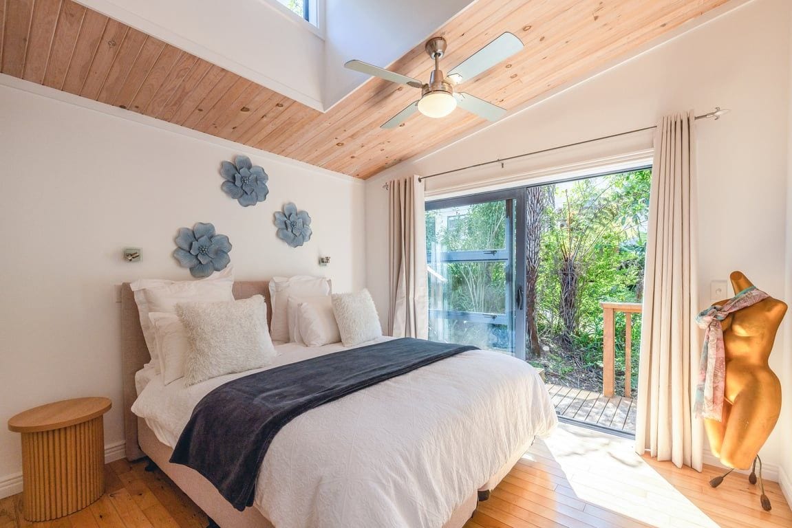 A bedroom with a bed, a ceiling fan, a window with curtains, and a view of greenery outside.
