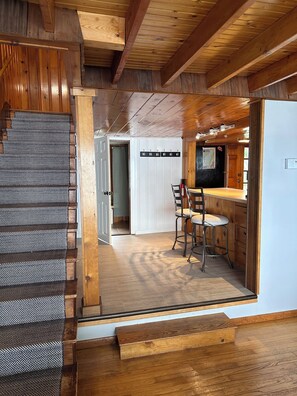 A wooden interior with a staircase, a bar area, and a seating arrangement. - Lakefront Maine Getaway - Private Dock & Kayaks (Burnham)