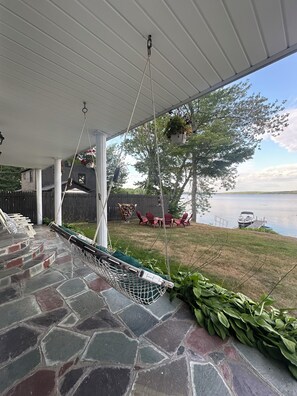 A covered porch with a hammock, stone flooring, outdoor furniture, and a view of a lake. - Lakefront Maine Getaway - Private Dock & Kayaks (Burnham)