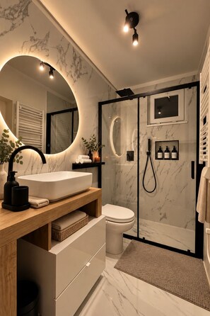 A modern bathroom with a marble sink, a toilet, a shower enclosure, and a large mirror. - Fiumicino Downtown Vacation Rental with Self-Check-In (Fiumicino)