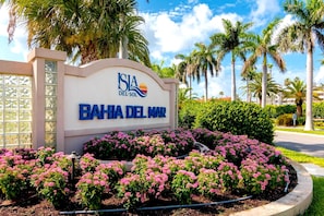 A sign for 'Bahia Del Mar' with a logo, surrounded by pink flowers and palm trees. - Endless Summer! Salty vibes only. (St. Petersburg)