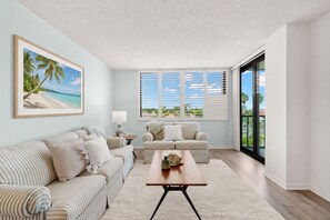 A living room with a sofa, armchair, coffee table, and a painting of a beach scene. - Endless Summer! Salty vibes only. (St. Petersburg)