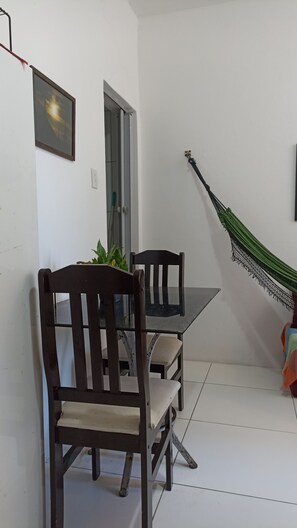 A dining area with a table and chairs, a hammock, and a door. - Apartamento na Barra (Salvador)