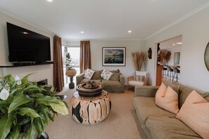 A living room with a flat-screen TV, a sofa, a coffee table, and a large plant. - The King Bali Retreat- Resort styled Sanctuary Balineese comforts kiwi lifestyle (Mangawhai)
