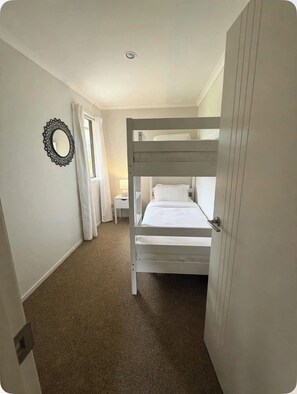 A bunk bed room with a white headboard, a bedside table with a lamp, and a wall mirror. - The King Bali Retreat- Resort styled Sanctuary Balineese comforts kiwi lifestyle (Mangawhai)