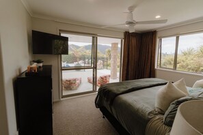 A bedroom with a bed, a television, a ceiling fan, and a balcony with a view of the outdoors. - The King Bali Retreat- Resort styled Sanctuary Balineese comforts kiwi lifestyle (Mangawhai)