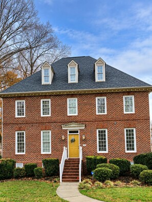 A two-story brick building with a central entrance, a yellow door, and a small porch with steps. - Nascar King Suite - 12 Mins to Speedway (Kannapolis)