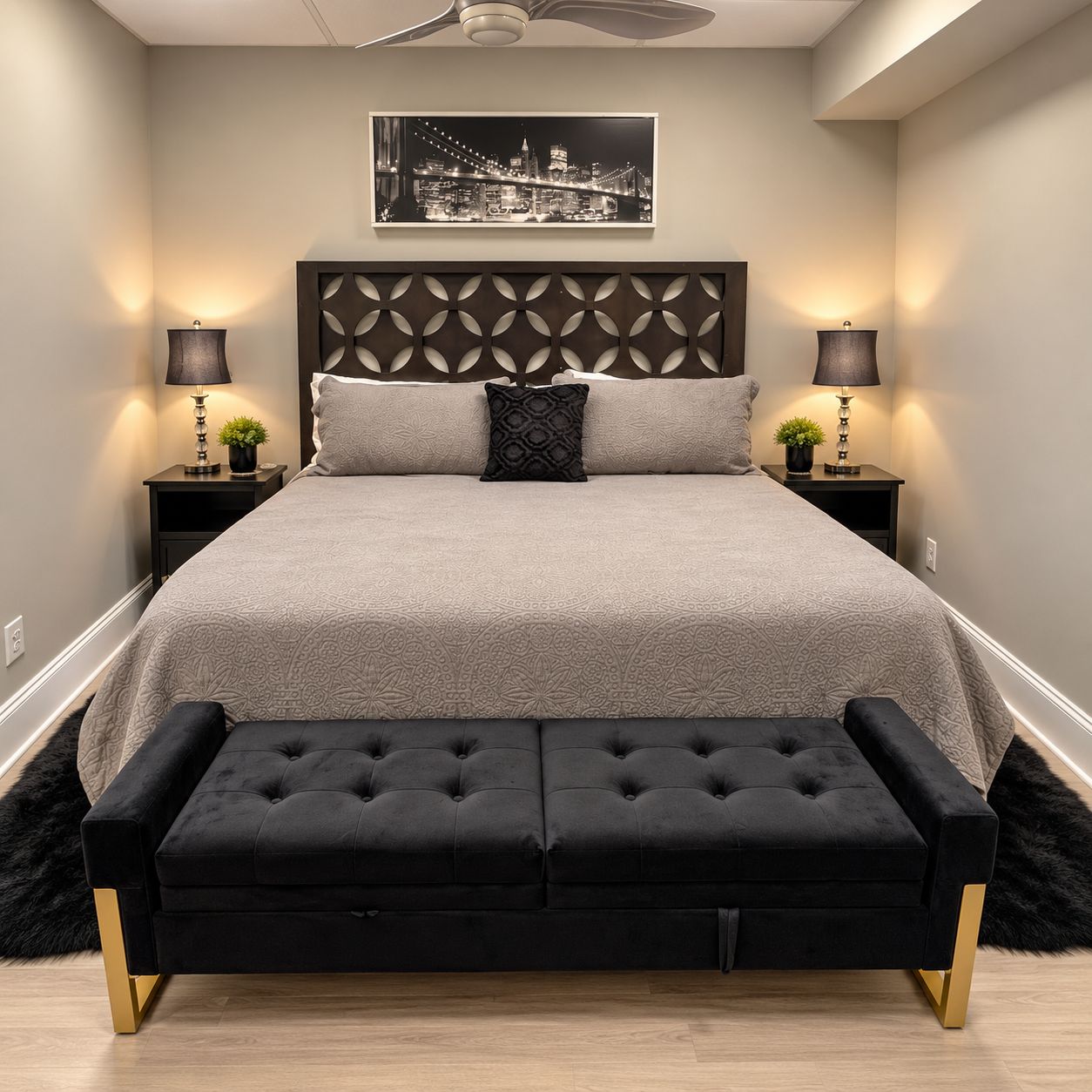 Ein modernes Schlafzimmer mit einer gesteppten schwarzen Couch, einem großen Bett mit gemustertem Kopfteil und zwei Nachttischen mit Lampen.