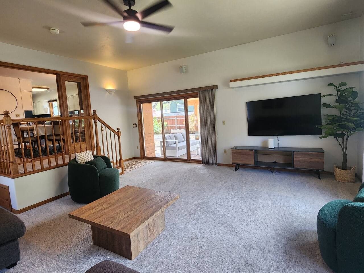 Una sala de estar amplia con una mesa de centro de madera, sofás verdes, un televisor de pantalla plana y una escalera que lleva a un balcón.