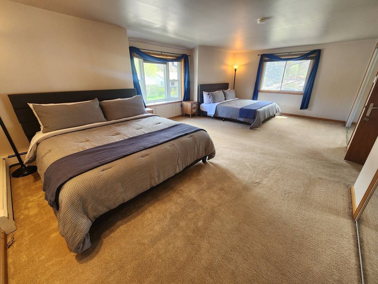 Un dormitorio con dos camas, piso alfombrado y una ventana con cortinas.