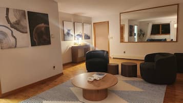 Een moderne woonkamer met een ronde houten salontafel, een zwart-wit gestreept vloerkleed en een zwarte leren bank.