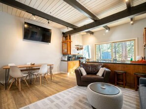 A modern kitchen with wooden cabinets, a dining area with a table and chairs, a leather sofa, and a large window providing a view of the outdoors. - 2BD/2BA Condo Near Bike Path/Shuttle Stop/Village/Lodges (Mammoth Lakes)