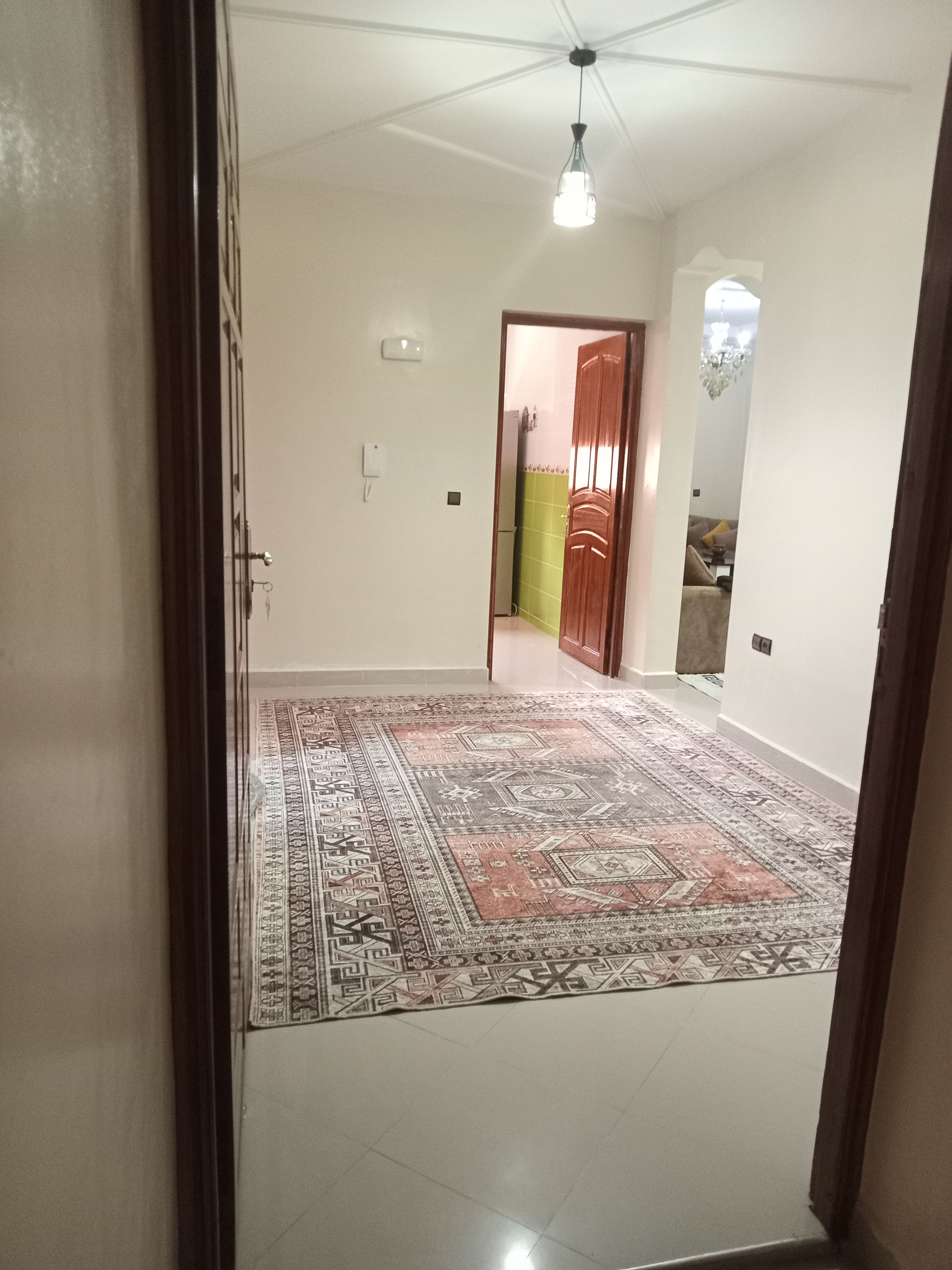 Una habitación amplia con alfombra estampada, un ventilador de techo y una puerta que da a otra habitación.