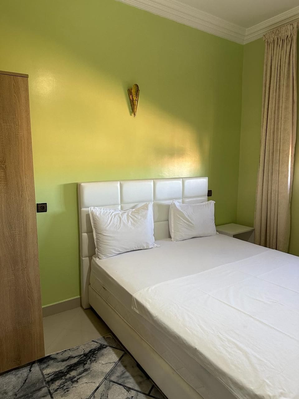 Ein Hotelzimmer mit einem großen Bett, einer Holztür und einer hellgrünen Wand.