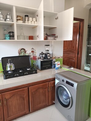 A compact kitchen with a stove, microwave, and washing machine. - RESIDENCE JANNAT (Ouarzazate)