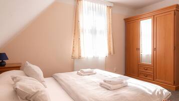 A bedroom with a bed, pillows, a nightstand, a wooden wardrobe, and a window with curtains.