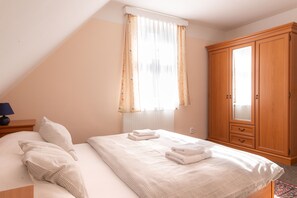 A bedroom with a bed, pillows, a nightstand, a wooden wardrobe, and a window with curtains. - Hamr Apartmány (Nové Hamry)