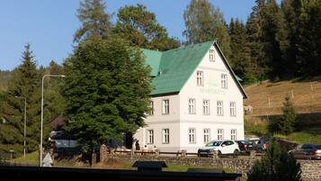 A two-story building with a green roof, labeled 'Harm's APARTMENT,' surrounded by trees and a stone wall.