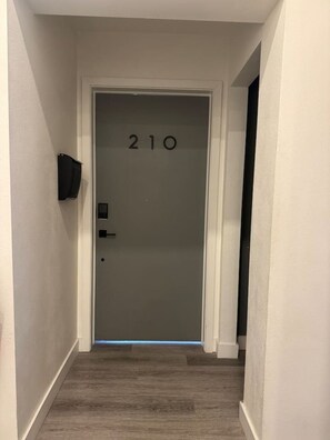 Ein Flur mit einer Tür, auf der '210' steht, und einem an der Wand befestigten Flachbildfernseher.