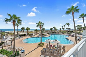 A pool area with lounge chairs and umbrellas, surrounded by palm trees and overlooking a beach. - Gulf Coast Beach Oasis Getaway (Gulf Shores)
