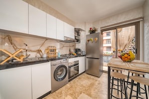 A compact kitchen with a washing machine, a refrigerator, and a dining area with a table and stools. - Luxury Moroccan Flat Near Carré Eden (Marrakesh)
