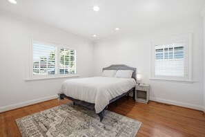 Een slaapkamer met een bed, nachtkastjes, een vloerkleed en ramen.