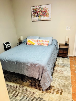 A bedroom with a bed, two bedside tables, a nightstand, a wall-mounted painting, and a patterned rug. - Charming 1-bedroom cottage in Ruston located perfectly for your convenience (Ruston)