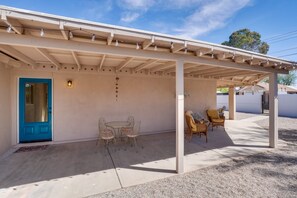 A covered patio with a table and chairs, a blue door, and a wall-mounted light fixture. - Spacious Tucson Retreat, Near UofA & Banner, Private Yard & Fire Pit (Tucson)