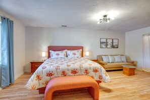 Quarto com cama, mesas de cabeceira, sofá, banco e luminária no teto.