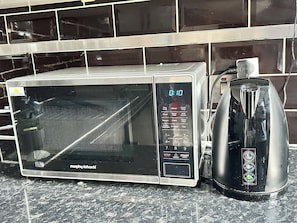 A microwave oven with a digital display and a coffee maker on a kitchen counter. - Smart Artistic 1-bedroom studio in Shoreditch London with stunning city views (London)