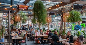 Un espace de restauration intérieur avec des tables et des chaises, des plantes suspendues et un plafond en verre.