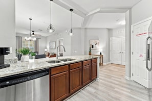 A modern kitchen with granite countertops, a dishwasher, wooden cabinets, and pendant lighting. - 3BR at Vista Cay, Where Comfort Meets Convenience (Orlando)