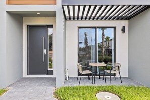 A modern outdoor patio with a glass door, a table with chairs, and a small garden area. - 3BR Near Disney, Harry Potter and Mickey Rooms (Kissimmee)