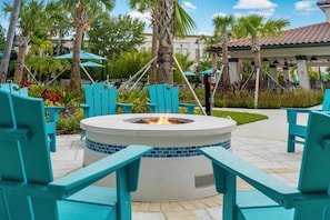 Een vuurplaats omringd door turquoise stoelen, palmbomen en een overdekt terras.