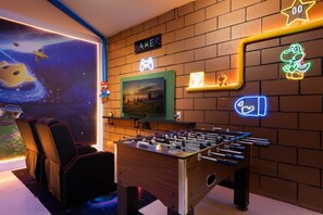 A room with a foosball table, a television, and a brick wall with neon signs. - 6BR Near Disney, Pool, Games and Themed Rooms (Kissimmee)