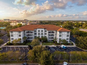 A multi-story residential building with a red-tiled roof, parking lot, and surrounding greenery. - Spacious 3BR Condo, Perfect Orlando Home Base (Orlando)