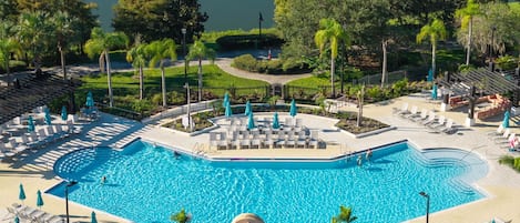 A large swimming pool with multiple lounge areas and sunbeds, surrounded by greenery and a view of the water.