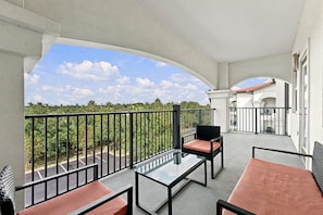 A balcony with a glass table and chairs, a view of a parking lot, and a building with a red-tiled roof. - Spacious 3BR Condo, Perfect Orlando Home Base (Orlando)
