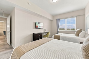 A hotel room with two beds, a desk, a chair, a TV, and a window with curtains. - Spacious 3BR Condo, Perfect Orlando Home Base (Orlando)