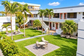A hotel courtyard with a central seating area, palm trees, and a staircase leading to the building's entrance. - Steps to Hollywood Beach - Modern 1BR Retreat (Hollywood)