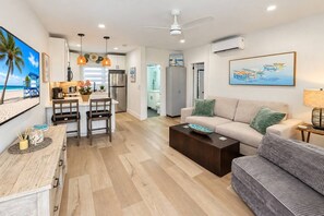 A modern living room with a sofa, coffee table, and a dining area with chairs and a kitchen in the background. - Steps to Hollywood Beach - Modern 1BR Retreat (Hollywood)
