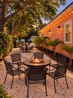 An outdoor patio with a round table and chairs, a fire pit, and a house with string lights. - Historic Home: Walk to Downtown, Jays & Waterfront (Dunedin)