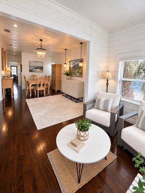 A spacious living room with a round coffee table, a sofa, and a dining area with wooden chairs. - Historic Home: Walk to Downtown, Jays & Waterfront (Dunedin)