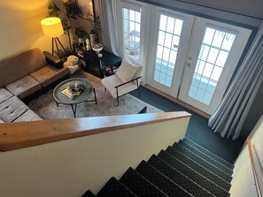 Un escalier menant à un espace de vie comprenant un canapé, une table basse et un fauteuil.