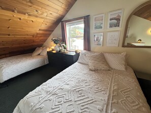 Une chambre avec deux lits, un plafond en bois, une fenêtre avec des rideaux et des tableaux encadrés accrochés au mur.