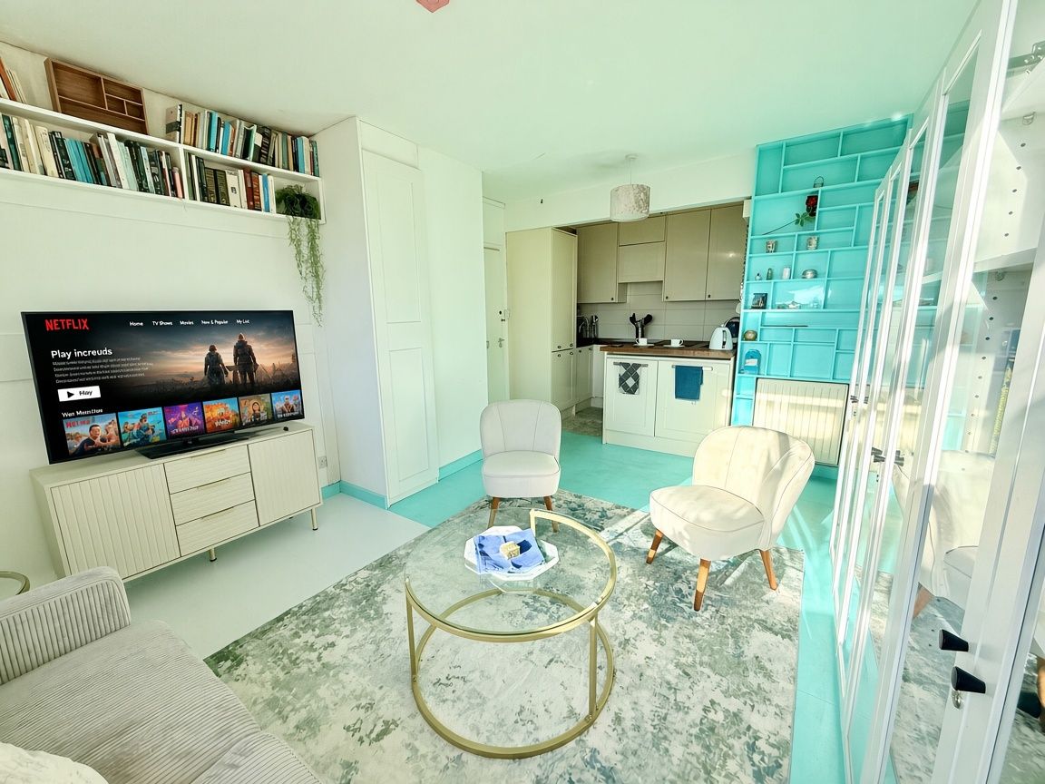 A modern living room with a flat-screen TV, a coffee table, and a bookshelf.