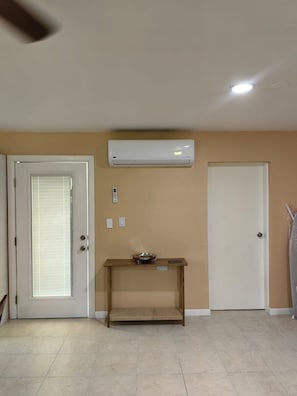 A room with beige walls, a white door with blinds, a white ceiling fan, and a white air conditioning unit mounted on the wall.