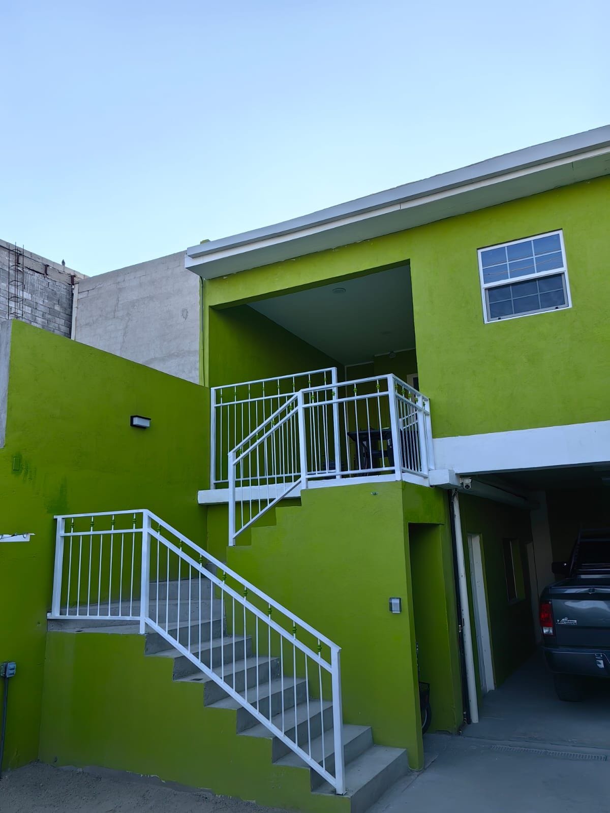 A two-story building with a green exterior, a white staircase, and a car parked in the driveway.