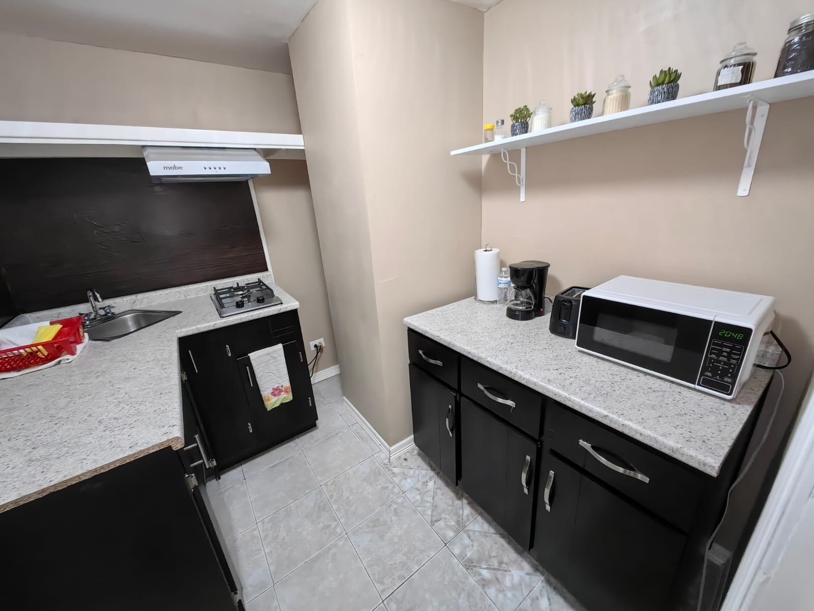 Una cocina compacta con estufa a gas, microondas, cafetera y una repisa con frascos.