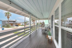 Eine überdachte Veranda mit Geländer, einem Hängesessel und einem Tisch mit Stühlen.